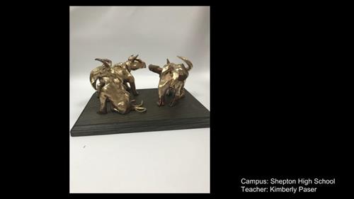 Two small sculptures of bulls with wings in a metallic gold finish.  